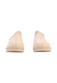 Paire de chaussures beige en daim sans lacets avec bordure tressée, vue de dos sur un fond blanc.