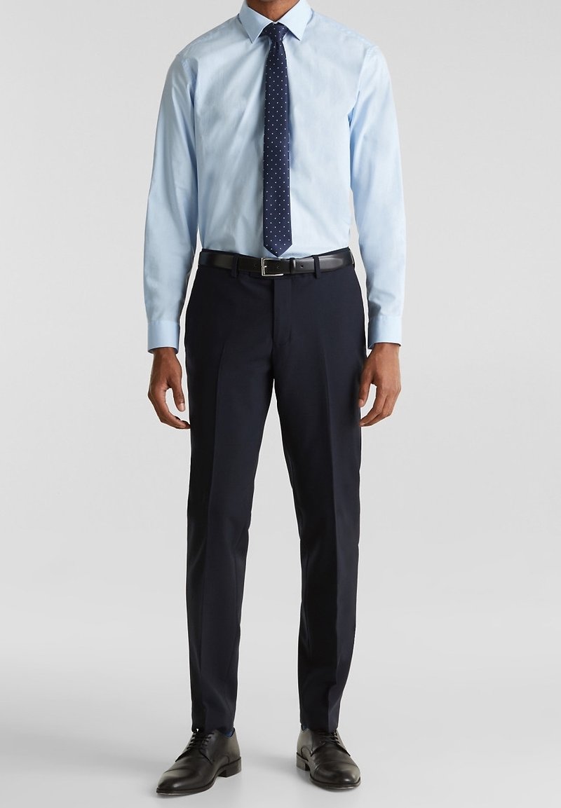 Ljusblå skjorta med spetsig krage, långa ärmar. Mörk marinblå slips med vita prickar. Mörka byxor och svarta skor. Enkelt mönster.