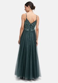 Zielona suknia w odcieniu szmaragdowym z misternym haftem koralikowym na bodice, z wycięciem w kształcie litery V z tyłu oraz warstwową spódnicą z tiulu z subtelnym blaskiem.