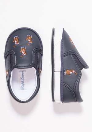 Granatowe wsuwane buty dziecięce z haftowanymi motywami gracza polo, białą podszewką oraz białymi gumowymi podeszwami z elastycznymi panelami po bokach.