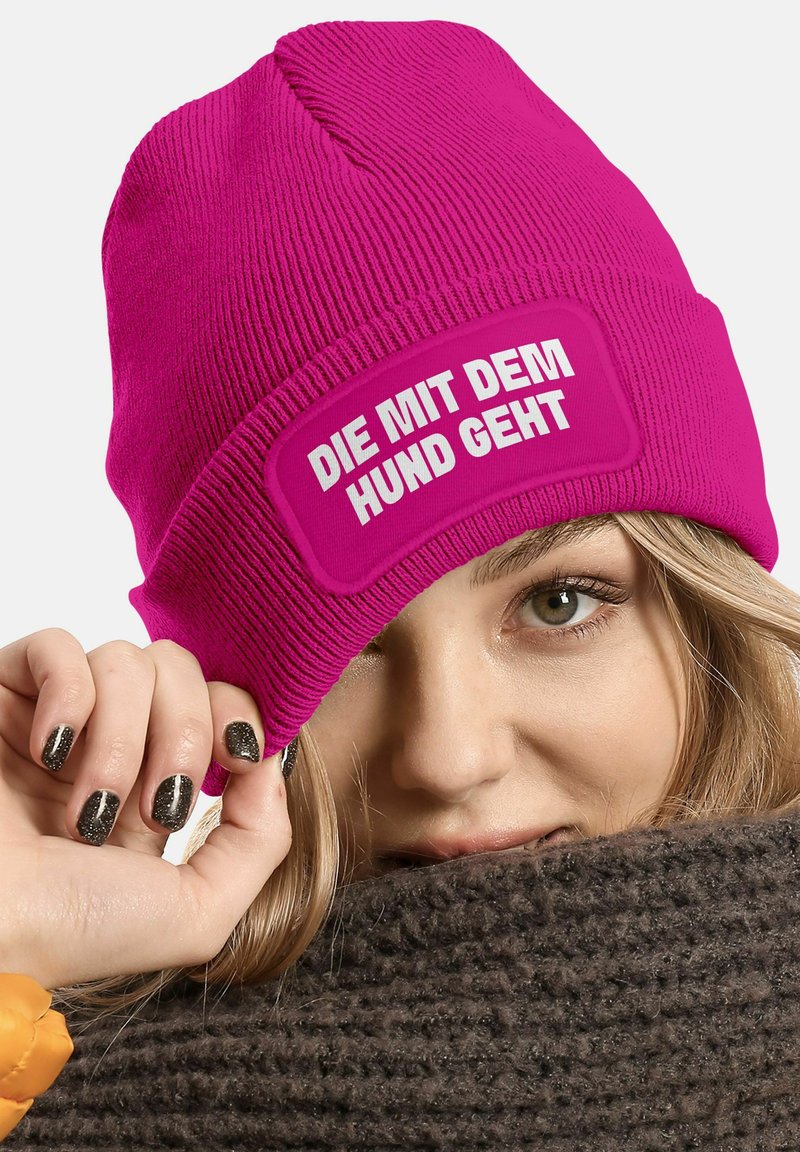 Fuchsia knitted beanie with a rectangular patch that reads "DIE MIT DEM HUND GEHT" in bold white text.