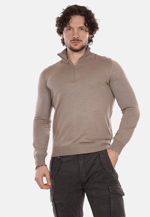 Maglione beige con zip e collo a imbuto, maniche lunghe, polsini e bordo a costine, realizzato in tessuto morbido. Il modello indossa pantaloni cargo scuri.