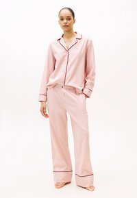 Set de pijama din bumbac roz deschis, compus dintr-o cămașă cu nasturi, cu borduri roșii, și pantaloni largi asortați, cu talie elastică.