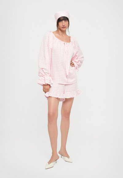 Ensemble de pyjama en vichy rose avec un ourlet volé, des manches longues et un bandeau assorti. Le tissu a une texture lisse. Les chaussures sont blanches avec des accents.