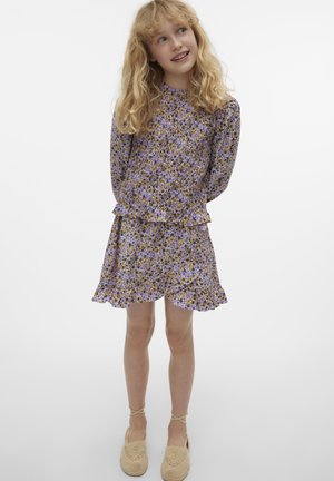 Vestido de estampado floral púrpura con dobladillo rizado y mangas abullonadas. Combinado con zapatos de rafia beige. Tela suave, textura ligera y aireada.