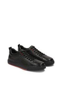 Sneaker in pelle nera con accenti rossi, pannelli texturizzati, punta rotonda e suola in gomma piatta. Lacci con occhielli metallici.