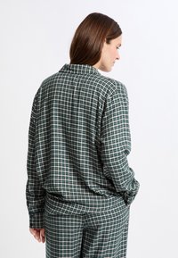 Sprawdzona flanelowa koszula w zielono-śmietankowym kolorze, z kołnierzem, długimi rękawami i luźnym krojem. Tekstura wydaje się miękka i wygodna.