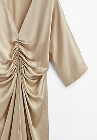 Robe en satin beige avec un décolleté en V profond, des manches larges aux coudes et un détail froncé à cordon au centre devant.