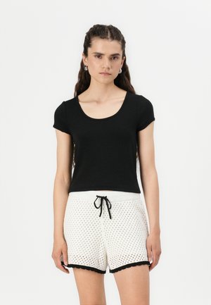 T-shirt noir à manches courtes avec un décolleté arrondi, associé à un short blanc avec une texture à motifs et un ourlet noir.