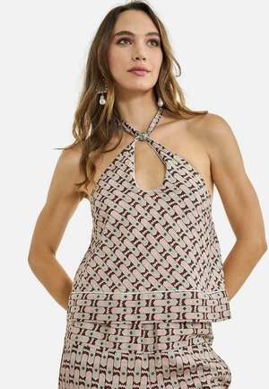 Mujer con top sin mangas de patrón y escote halter con abertura en la parte delantera, falda a juego, complementada con pendientes colgantes de perlas.