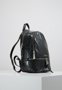 Zaino sintetico nero con finitura lucida, due scomparti con zip, motivo del logo e spallacci regolabili. Dettagli in metallo lucido.