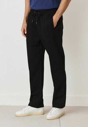 Black sweatpants with an elastic waistband and drawstring. Features side pockets and a straight leg design, paired with white sneakers.