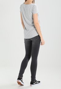 Šedé bavlněné tričko s krátkými rukávy, spárované s černými skinny džíny a černými teniskami s bílou podrážkou, ukazující volnočasový outfit.