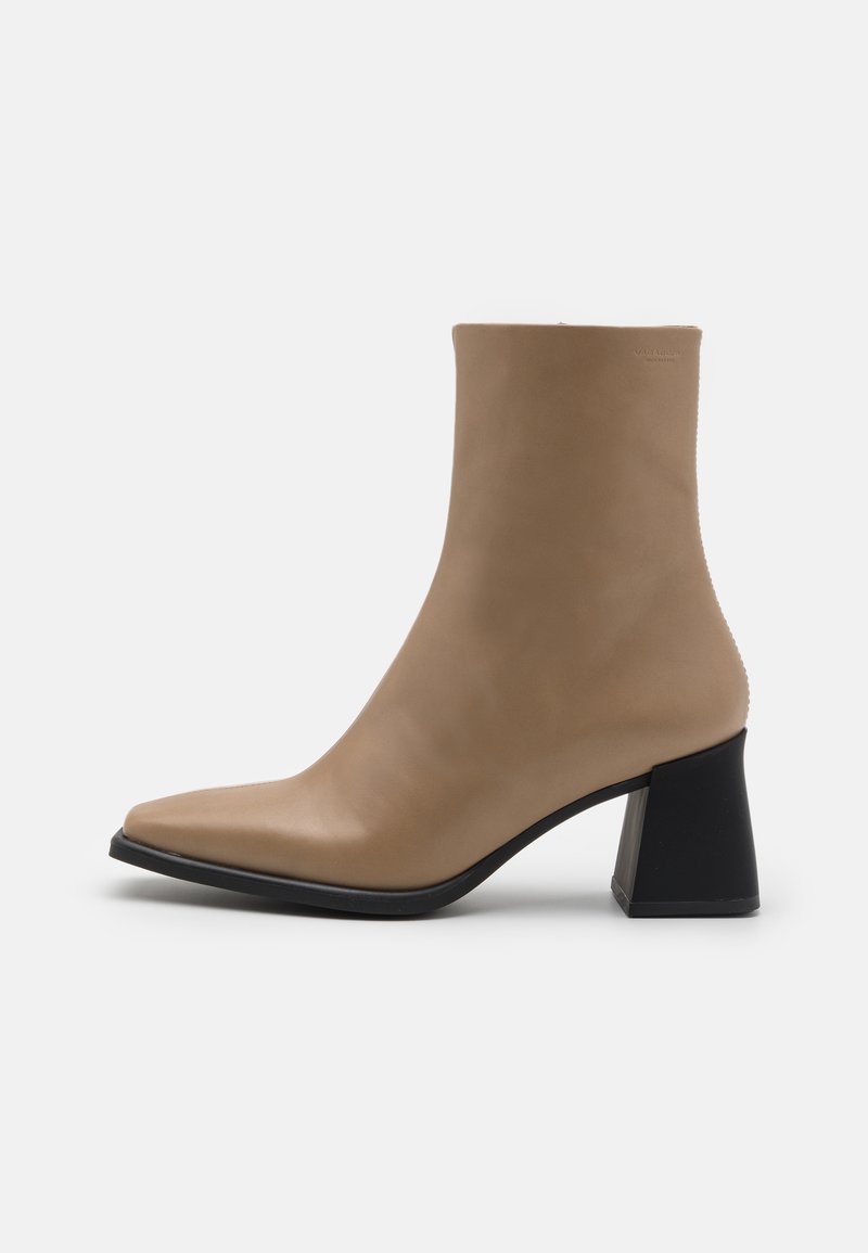 Bottine en cuir beige avec un bout pointu et un talon noir épais, présentant une texture lisse et un design minimaliste.