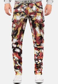 Pantalons cargo multicolores présentant un motif éclaboussé de peinture en rouge, jaune et noir, avec plusieurs zippers et des accents cloutés.