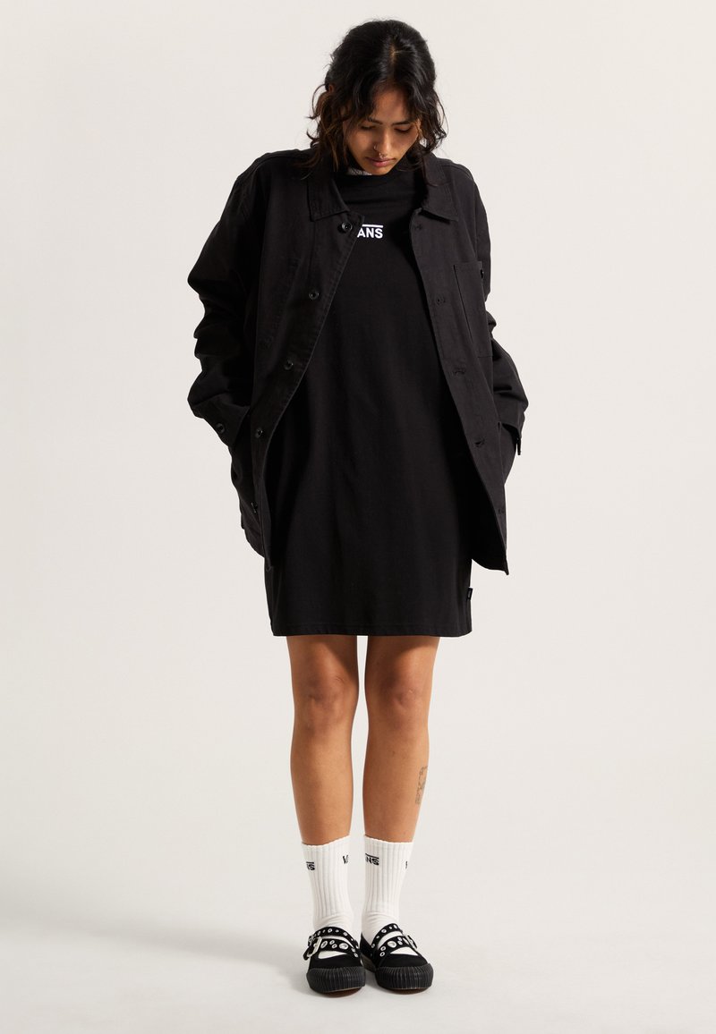 Veste en jean noire, robe t-shirt noire, chaussettes blanches à hauteur de cheville et chaussures noires avec des accents circulaires. Design minimaliste, coupe décontractée.