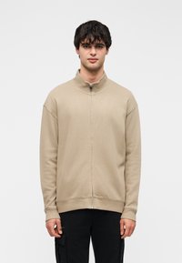 Μπεζ φούτερ με φερμουάρ, ψηλό γιακά, ριμπ μανσέτες και ίσια τελική ράχη. Με λεία υφή και άνετη εφαρμογή.