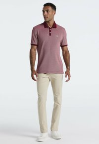 Polo à manches courtes bordeaux avec un col contrastant, deux boutons et un tissu texturé. Associé à un pantalon couleur crème et des baskets blanches.