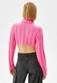 Rosa kortärmad tröja med ribbat mönster, hög krage och långa ärmar, ihop med mörkgrå högmidjade byxor med fickor.