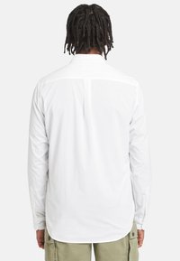 Witte longsleeve shirt met knoopmanchetten, achterste yoke details, rechte zoom en gladde textuur, gecombineerd met olijfgroene cargobroek.