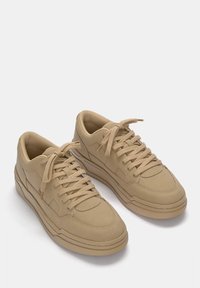 Zapatillas beige con parte superior sintética lisa, puntera redonda, cordones tono sobre tono y un diseño de suela sobredimensionada. Presentan costuras sutiles y detalles de paneles.