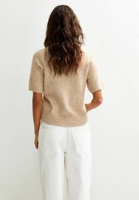 Beige kortere mouwtrui van zacht gebreid materiaal met een geribbeld zoom, gecombineerd met witte hoge taille broeken met twee achterzakken.