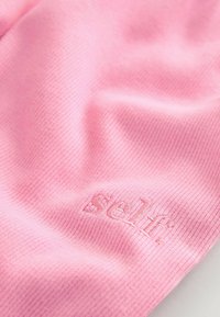 Tessuto ribbed rosa con una morbida texture, caratterizzato dal logo ricamato "self." in una tonalità abbinata vicino all'angolo in basso a destra.