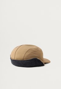Gorra marrón con una suave orejera forrada de piel negra, con una parte superior redondeada y una visera curva, fabricada con un tejido suave.