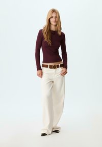 Burgundy long-sleeve shirt paired with loose-fitting white pants and a brown belt featuring a gold circular buckle. Black pointed-toe shoes.