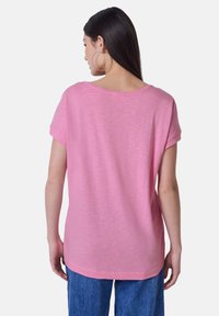 Růžový top s krátkým rukávem a kulatým výstřihem, vyrobený z lehkého materiálu. Zadní část je mírně delší a má volnější střih.