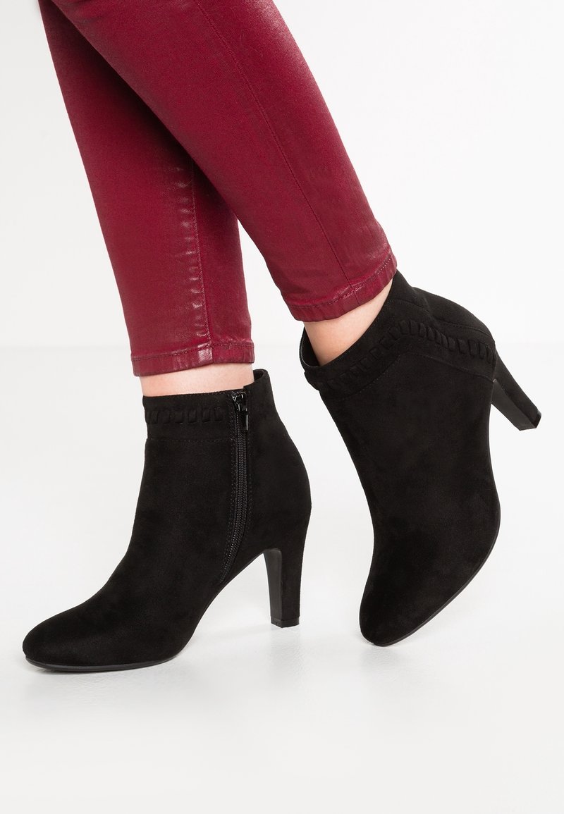 Botines de ante negros con tacón delgado y cremallera lateral, con un borde texturizado en la parte superior. Combinados con pantalones slim burdeos.