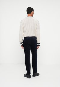 Witte textuur gebreide trui met geribbelde boorden, gecombineerd met donkere marineblauwe broek. Casual schoeisel maakt de outfit compleet. Achteraanzicht.