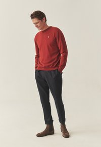 Pull rouge à col rond en matière tricotée douce. Assorti à un pantalon bleu marine et des bottines marron avec une finition lisse.