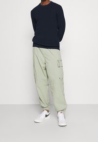 Jersey de marina con ribetes de canalé, combinado con pantalones cargo verde claro con bolsillos y zapatillas blancas con detalles negros.