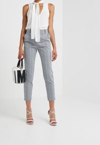Blusa bianca con un nodo al collo, abbinata a pantaloni attillati a scacchi in bianco e nero. Accessoriata con una piccola borsa audace e con sandali con cinturino.