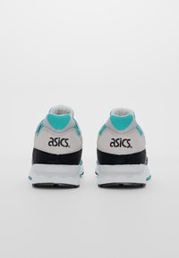 Ett par Asics-sneakers i teal, svart och vitt visade bakifrån på en enfärgad vit bakgrund.