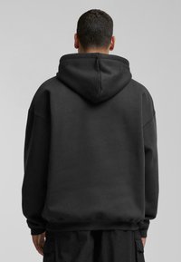 Black oversized hoodie made from a soft fabric. Features a large hood, dropped shoulders, and ribbed cuffs and hem. Simple design.