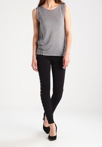 Szary bezrękawnik z ozdobnymi wstawkami z boku, połączony z czarnymi legginsami z guzikami po bokach i wykończony czarnymi szpilkami.