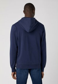 Granatowy hoodie wykonany z miękkiego materiału, z kapturem na sznurku, ściągaczami przy mankietach i w pasie oraz luźnym krojem. Pokazano widok z tyłu.