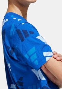 Maglietta blu in cotone con un design grafico che presenta diverse sfumature di blu e forme geometriche nere che si estendono su tutto il tessuto.