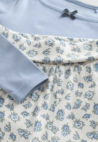 Robe fleurie avec un haut côtelé bleu clair et une jupe à motifs présentant de petites fleurs bleues sur un fond crème. Finition avec un détail nœud.