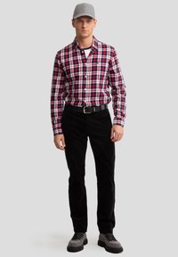 Chemise à carreaux rouge, blanche et bleue ; pantalon en velours côtelé noir ; casquette grise ; bottes grises et noires avec semelles texturées.
