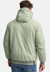 Mint green padded jacket with a tall hood, ribbed cuffs, and hem. The fabric has a subtle texture. Features a small brown accent tag on the side.