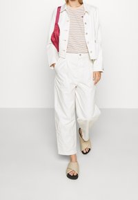 Vit denimjacka över en randig skjorta, ihop med högmidjade vita byxor och beige sandaler med korskälk. Rosa väska som accent.