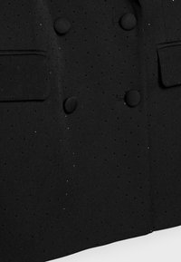 Schwarzer zweireihiger Blazer aus strukturiertem Stoff mit kleinen Perforationen. Zwei Vordertaschen und runde, strukturierte Knöpfe.