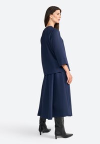 Námorně modrý dvoudílný outfit se volně padnoucím topem s 3/4 rukávy a splývavou sukní, doplněný černými botami na podpatku se špičatou špičkou.