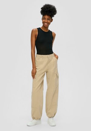 Black ribbed sleeveless top paired with loose, beige cargo pants featuring side pockets and elastic cuffs, worn with white sneakers.