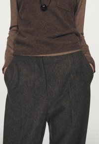 Brown knit sweater with long sleeves. Paired with dark gray, textured tailored trousers featuring pleats and side pockets.