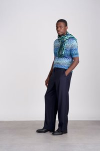 Πλεκτό μπλε πουλόβερ κοντομάνικο με σχέδιο ζιγκ-ζαγκ, σε συνδυασμό με σκούρα μπλε παντελόνι με ρίγες και πράσινο κασκόλ με σχέδιο. Μαύρα παπούτσια ολοκληρώνουν την εμφάνιση.