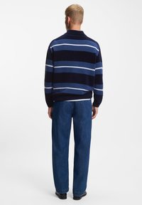 Navy striped knit pullover with blue and white stripes, textured fabric, collared design, paired with straight-leg denim trousers.